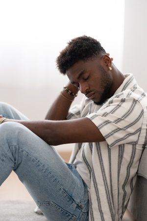 Sad african american man sitting on the floor and thinking. Black person suffering depression.の写真素材