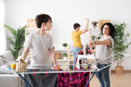Family doing laundry, ironing and cleaning the house. Mother giving instructions to teenager son. Equality conceptの写真素材