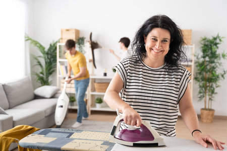 Woman ironing clothes while looking and smiling at camera. Family doing housework.の写真素材