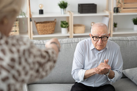 Unrecognizable woman menacing submissive elderly man. Senior man asking for forgiveness.の写真素材