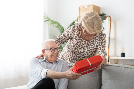 Senior man receiving present from wife at valentine's day. Woman giving gift to elderly husbandの写真素材