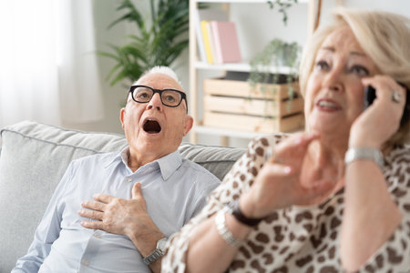 Senior man suffering heart attack and worried woman making emergency call. Elderly health problems conceptの写真素材