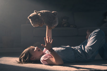 Child playing and talking to plush toy. Little girl holding teddy bear with sunset light at home.の写真素材
