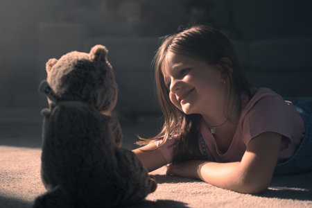 Closeup of happy little girl playing with teddy bear with dramatic backlightの写真素材