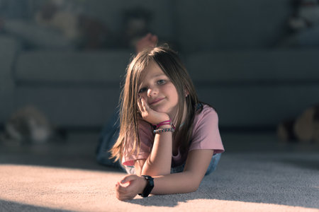 Portrait of little girl lying on the floor and looking at camera. Child in sunset light indoorsの写真素材