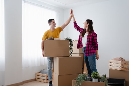 Happy young couple giving high five surrounded by carton boxes. Moving home concept.