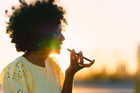 Rays of the sun illuminating an african woman sending a voice messageの写真素材