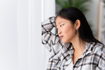 Close-up photo of a sad woman looking out the window at homeの写真素材