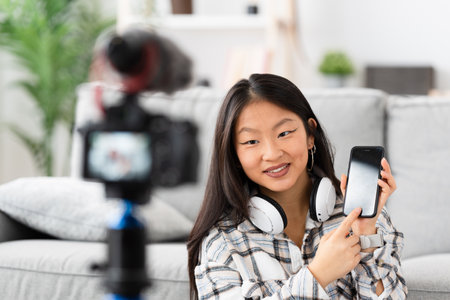 Chinese woman recording a video tutorial at home using a camera and showing a mobile phone