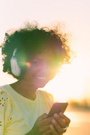 Vertical photo of the rays of the sun illuminating an african woman listening to music outdoors