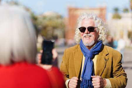 Senior woman taking a portrait on the phone to husband. Mature man posing to camera outdoors.の写真素材