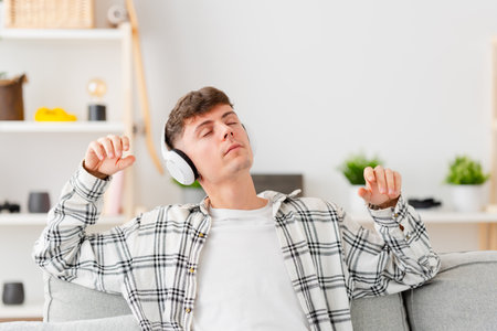 Teenager boy listening relaxing music on headphones sitting on sofa