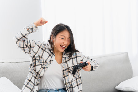 Happy chinese woman celebrating that wins in console game sitting on the sofa at home