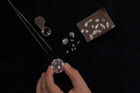 Top view of Diamonds of different cuts and sizes scattered on table with a magnifying glass and...