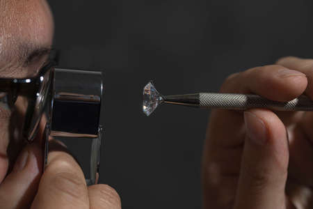 Close up of asian male diamond dealer buyer expert evaluates polished diamonds at exhibition. High...