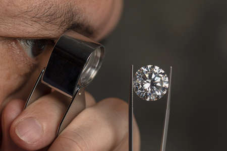 Close up of asian male diamond dealer buyer expert evaluates polished diamonds at exhibition. High...