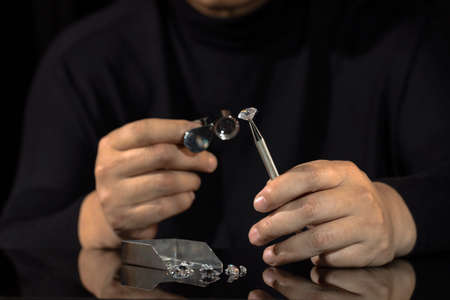 Close up of asian male diamond dealer buyer expert evaluates polished diamonds at exhibition. High...