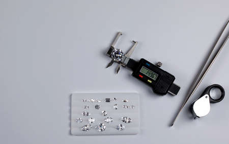 layout of jewelry tools and diamond of different cuts and sizes on white platform for comparing the...