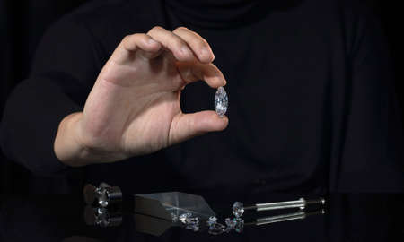 Close up of Marquis cut diamond in the hand of jewelry expert evaluating diamonds on black...