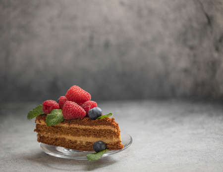 Slice of honey cake decorated with raspberries and blueberries with fresh mint leaves. Top view on gray background. Content for food bloggers with copy space. High quality photoの写真素材