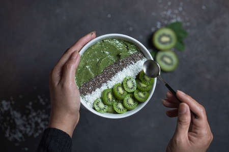 Close up of green healthy fresh spinach kiwi smoothy in bowl with berry kiwi topping with chia seeds and coconut flakes. Detox dieting, clean eating, vegan food concept. Top view with copy space.の写真素材