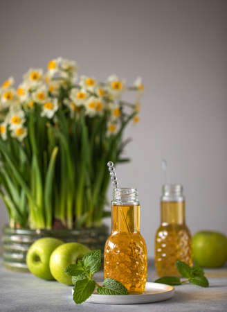 Close up of fresh apple juice in bottles on table with green apples mint and bouquet of daffodils. Fresh healthy drink. High quality photoの写真素材
