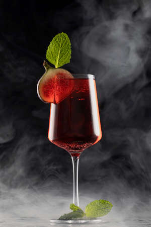 Glass of red drink decorated with slice of figs and mint leaf on black background with frozen water drops and smoke. High quality photoの写真素材