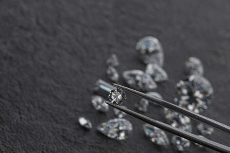 Polished diamonds of various shapes and sizes at workplace of jewelry expert evaluating the quality of stones on dark background with copy space. High quality photoの写真素材