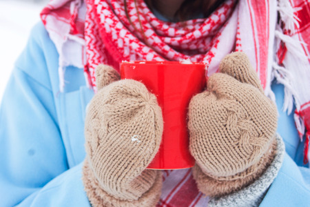 the girl in mittens holds a red cup in handの写真素材