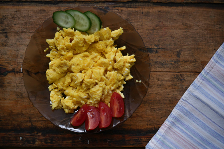 Scrambled eggs, slices of tomato and cucumber in a plateの写真素材
