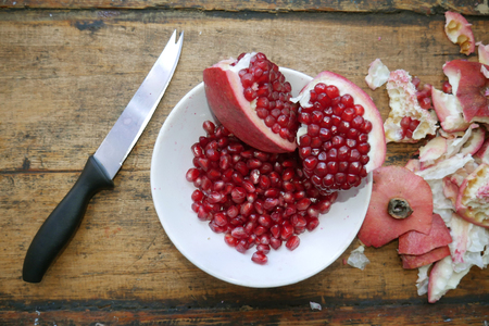 sliced pomegranate and pomegranate fruits in a white plate next to a knife and a peel from pomegranateの写真素材