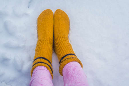 Female legs in warm pink pants and yellow socks on a snow background outdoors