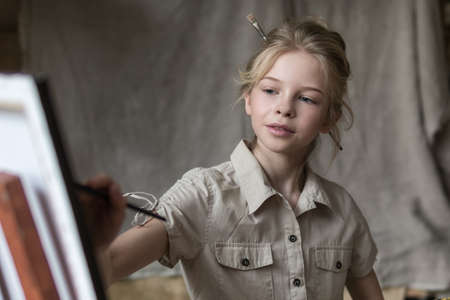 Girl with brushes near easel with picture of flowers in interiorの写真素材