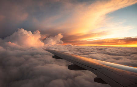 An airplane wing, many thick clouds, pink-orange sky, sunset. A long awaited journey.の写真素材