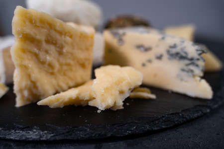 Parmesan and gorgonzola are on a black wooden plate. Tasting of delicious cheeses. Fermented milk...