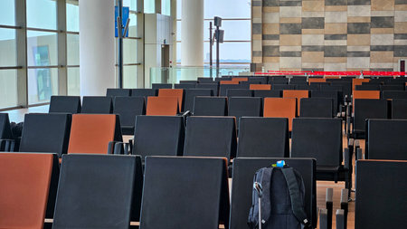 Peaceful empty airport waiting area with rows of seats, wooden floor, bright sunlight streaming...