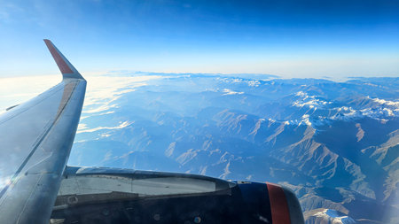 Aerial shot from airplane window showing wing, clouds, and the landscape below. A symbol of exploration and discoveryの写真素材