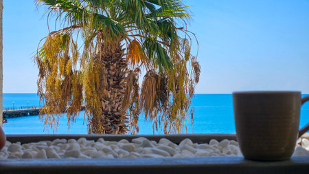 A ceramic cup on white pebbles with a palm tree and turquoise sea in the backgroundの写真素材