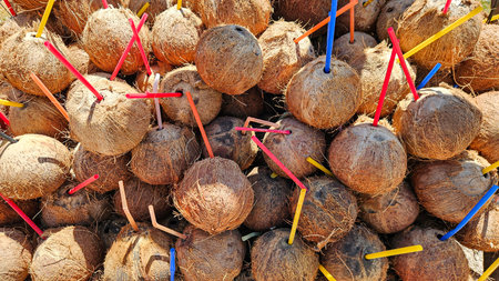 Stack of ripe coconuts with colorful straws at a sunny tropical market. Perfect for summer, travel, and exotic drink conceptsの写真素材
