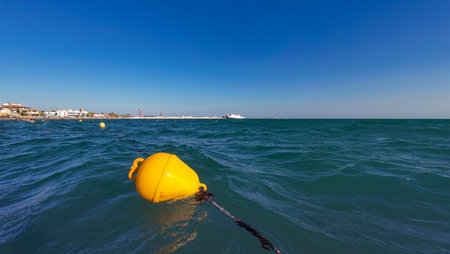 Bright yellow buoy floating on turquoise wavy sea under clear blue sky. Marine navigation concept...