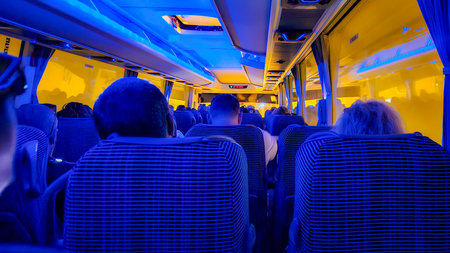 Passengers seated inside a long distance bus at night with blue ambient lighting representing...
