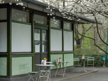 A picturesque outdoor cafe scene unfolds under a blossoming tree, inviting relaxation and enjoyment with its charming design and vibrant floral accents.の素材