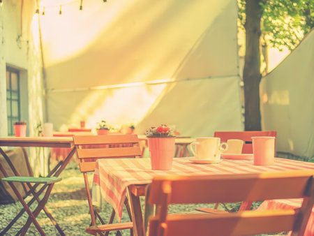 An inviting outdoor cafe scene with a wooden table and checkered tablecloth basks in natural light, creating a tranquil and relaxed atmosphere, perfect for hospitality and leisure concepts.の素材