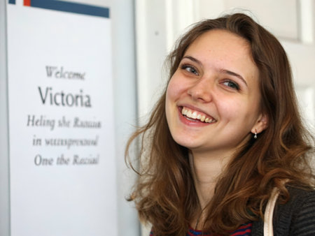 A smiling young woman stands as a symbol of inclusivity in Wisconsin, captured in a warm and inviting indoor setting. The banner behind her promotes a message of diversity and welcomes Victoria Heling, referencing a "Rainbow" initiative within the state.の素材