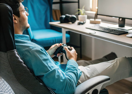 A person intensely plays a video game at a cluttered desk, illuminated by natural light. The scene conveys a sense of concentration and leisure, highlighting the immersive experience of modern gaming.の素材