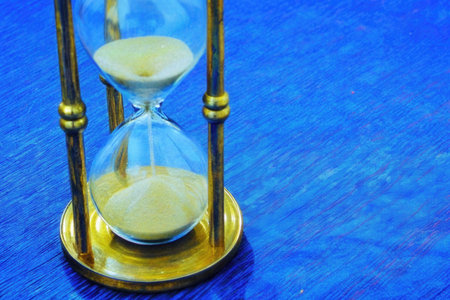 Hourglass on blue background. Sand running through the glass. Time passing conceptの素材