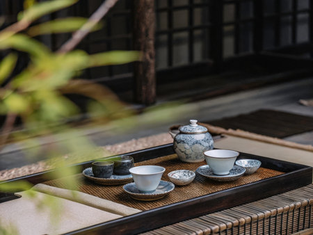 A beautifully arranged tea set featuring intricate blue floral teapots, cups, and saucers rests on a dark woven tray, creating a serene and sophisticated composition.の素材