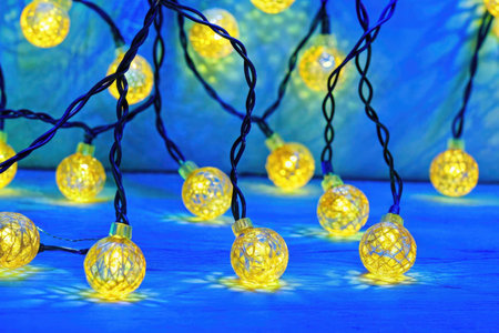 Glowing yellow christmas lights on a blue background. Close upの素材
