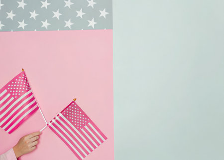 Woman hand holding American flag on pink and blue background. Flat lay, top view.の素材