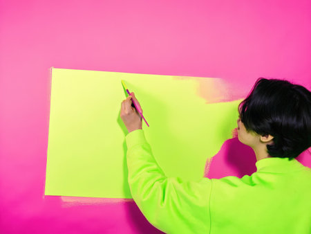 A young artist intensely focuses on a large green sketchpad, utilizing a lime green sweatshirt and pencil. The image radiates creativity and energy, showcasing an artistic moment captured in a bright, dynamic setting.の素材